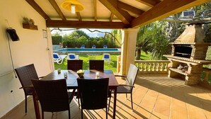 Un pati exterior amb taula i cadira, una barbacoa i vista a una piscina.