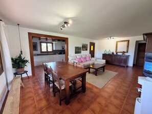 A spacious living area with a wooden dining table, a sofa, and a kitchen in the background.
