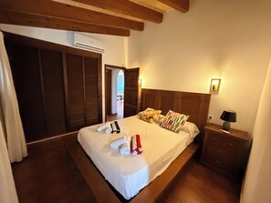 A hotel room with a large bed, wooden headboard, a bedside table with a lamp, and an air conditioning unit.