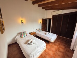 A hotel room with two beds, a wooden ceiling, an air conditioning unit, and a view of a building through a window.