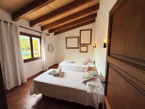 A hotel room with two beds, a large window with curtains, a wooden ceiling, and a view of a swimming pool. - Villa Cal Roma with swiming pool in the countryside (Pollensa)