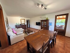 A spacious living area with a wooden dining table, a sofa, and a television mounted on the wall.