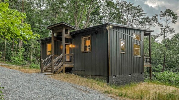 Escape to a cozy cabin nestled in the forest, featuring a rustic design and a welcoming porch with a staircase leading to the entrance.