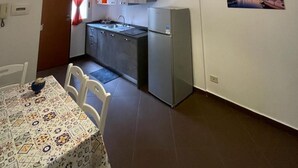 A compact kitchen with a refrigerator, a dining table with chairs, and a hanging pendant light. - CALA APARTAMENT (Palermo)