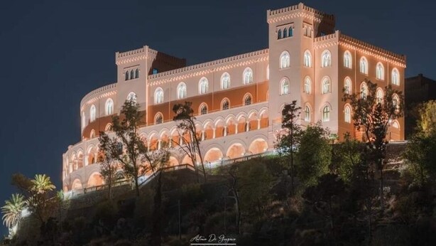 A large, illuminated building with multiple arches and a tower, surrounded by trees. - CALA APARTAMENT (Palermo)