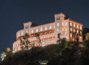 A large, illuminated building with multiple arches and a tower, surrounded by trees. - CALA APARTAMENT (Palermo)