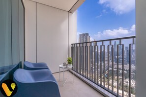 A balcony with a city view, a small table with a plant, and blue chairs. - Vogue | Downtown with Direct Access to Dubai Mall (Dubai)