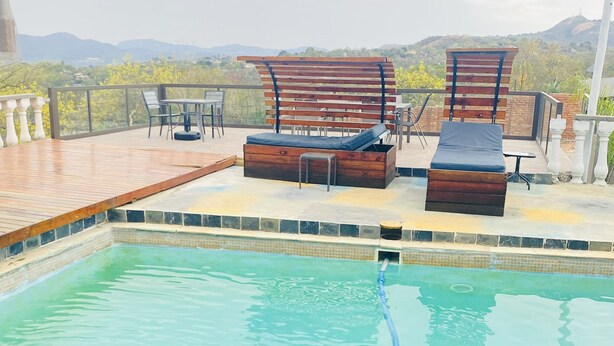 A rooftop pool with wooden deck, lounge chairs, and a table. - Full Moon Guest House (Mbombela)
