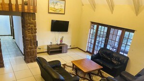 A living room with a black leather sofa set, a wooden coffee table, and a flat-screen TV mounted on the wall. - Full Moon Guest House (Mbombela)