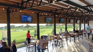 Un espacio de estar al aire libre cubierto con mesas y sillas, con vista a un campo de golf.