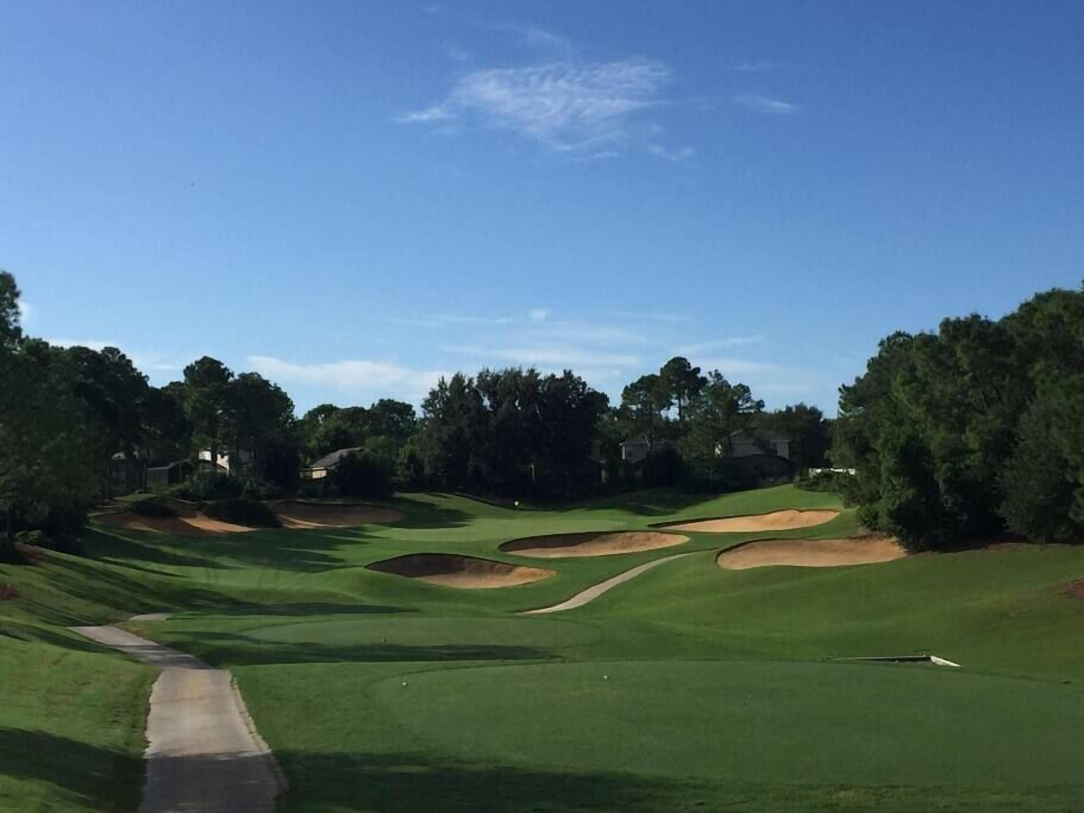 Un campo de golf con un camino despejado, búnkeres de arena y árboles.