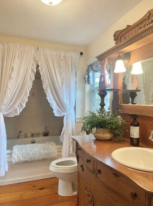 Un baño con bañera, inodoro y tocador con espejo y lavamanos.