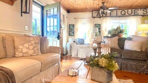 Un salon chaleureux avec un canapé beige, une table basse en bois et une enseigne indiquant « ANTIQUITES ».