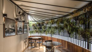 A covered outdoor seating area with tables and chairs, a wooden bench, and a wall of hanging plants. - Estúdio Aconchegante, Metrô, Piscina, Sauna, AC (São Paulo)