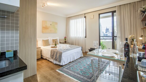 A modern hotel room with a large bed, a dining area, and a view of the cityscape. - Estúdio Aconchegante, Metrô, Piscina, Sauna, AC (São Paulo)
