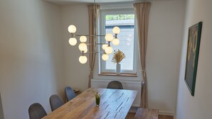Ein Essbereich mit Holztisch, weißen Stühlen, einer Bank und einer Pendelleuchte.