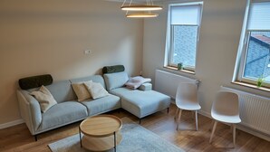 Ein modernes Wohnzimmer mit einem grauen Ecksofa, einem runden Couchtisch aus Holz und einem weißen Sessel.