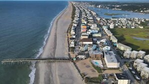 Vue aérienne d’une zone résidentielle côtière, avec une plage, des maisons et une jetée.