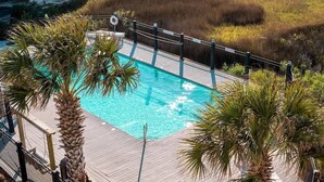 Une piscine avec une terrasse en bois, entourée de palmiers et délimitée par une clôture.