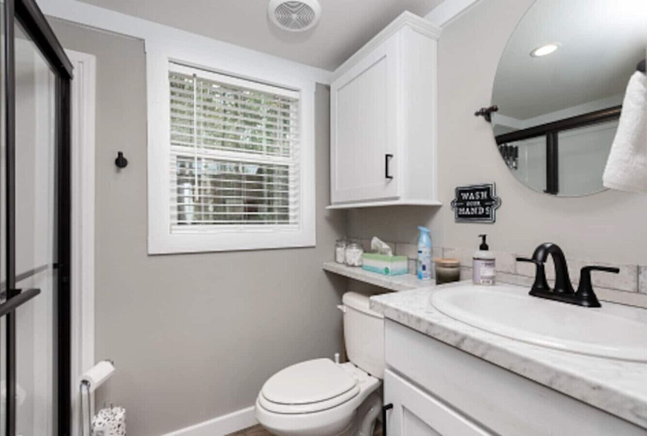 A bathroom with a toilet, sink, and window. There is a sign on the wall that says "WASH HANDS."