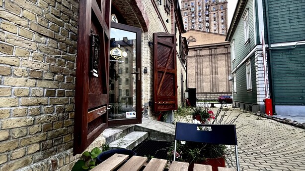 Un banc en bois, une tasse blanche, un bâtiment en briques et, au loin, une vue sur une haute tour.