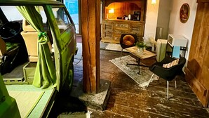 Un intérieur rustique avec des poutres apparentes, une voiture verte, une cheminée et un coin salon confortable.