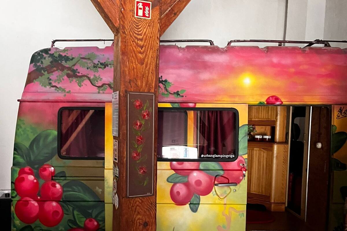 En husbil med en iögonfallande, fruktinspirerad design på utsidan, en brandsläckare som är monterad på en trästolpe och ett bord med ett bordsduk som har ett lövmönster.