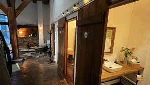 Un couloir étroit, doté d’un plancher en bois et de poutres apparentes, mène à une salle de bain avec un meuble-lavabo en bois et un évier.