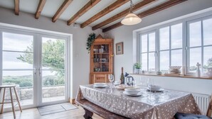A dining area with a wooden table set for four, a bench, and a view through large windows.