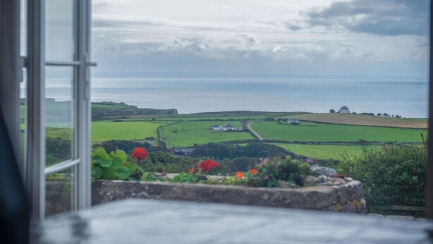 A view from a window overlooking a coastal landscape with fields and a distant house.
