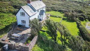 A white house with a sloped roof, a stone wall, and a grassy yard.