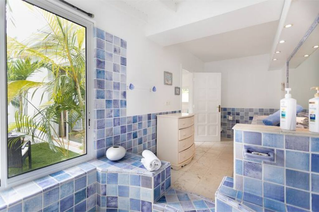 Een badkamer met blauwe tegels, een witte wastafel en een raam met uitzicht op palmbomen.