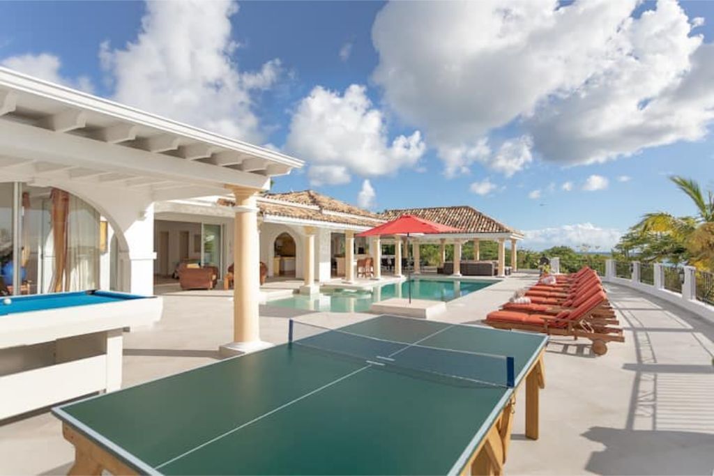 A pool area with a ping pong table, lounge chairs, and a covered seating area.