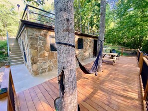 A wooden deck with a stone building, a hammock, and a picnic table.
