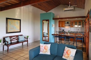 A spacious living area with a blue sofa, wooden bench, and a kitchen in the background.