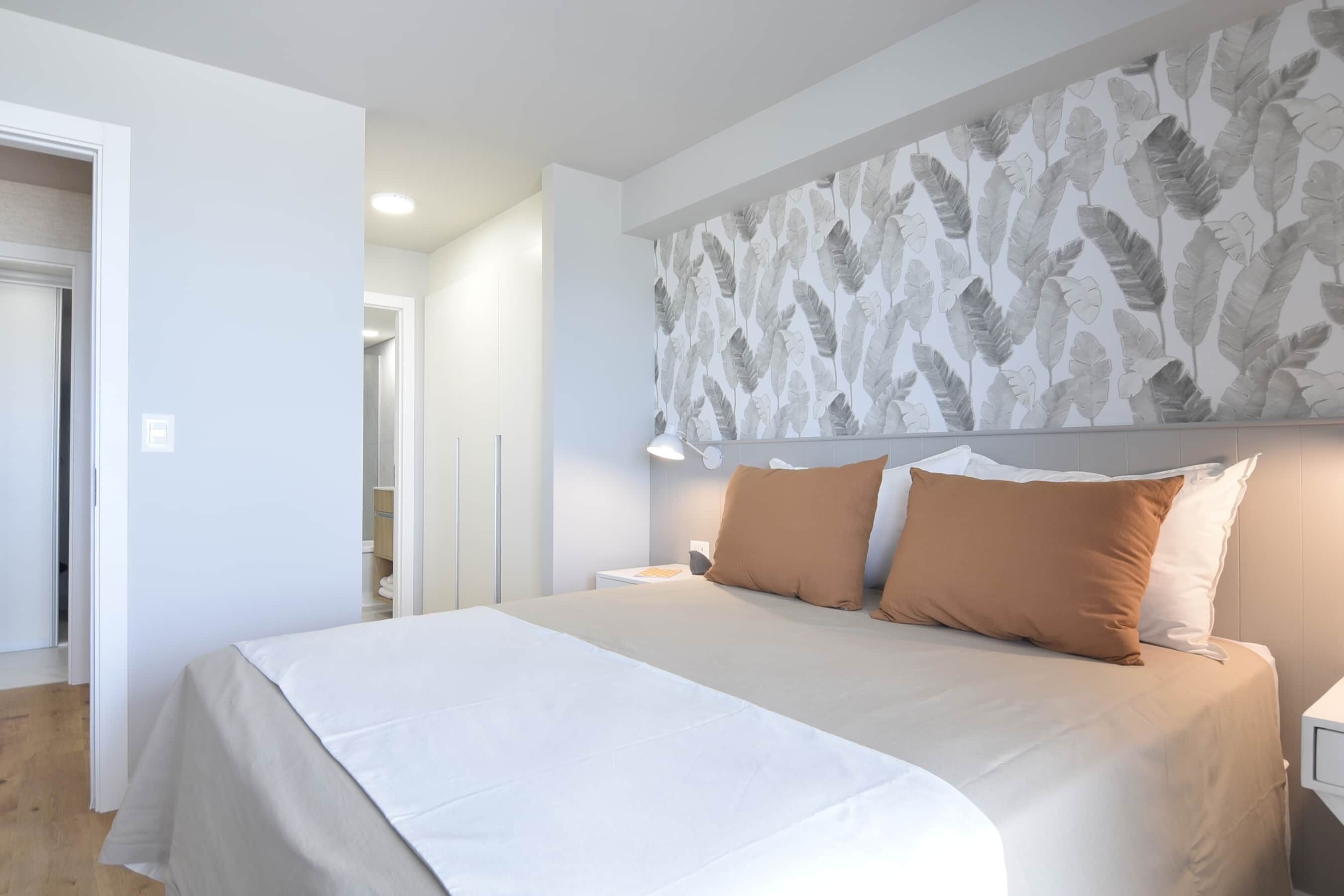 A bedroom with a large bed, white bedding, a headboard with a leaf pattern, and a nightstand with a lamp.