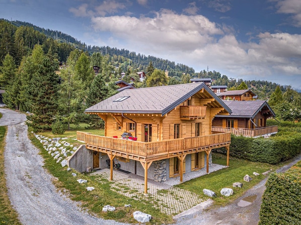 A wooden chalet with a balcony, surrounded by a forested landscape.