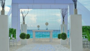 A beach wedding setup with a white archway, a table with spherical decorations, and chairs. - The Sens Riviera By Oasis (Akumal)