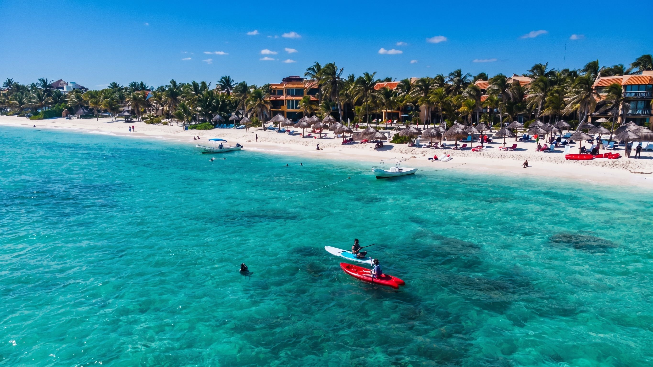 Una playa con aguas turquesas cristalinas, una orilla arenosa y una hilera de edificios con palmeras.