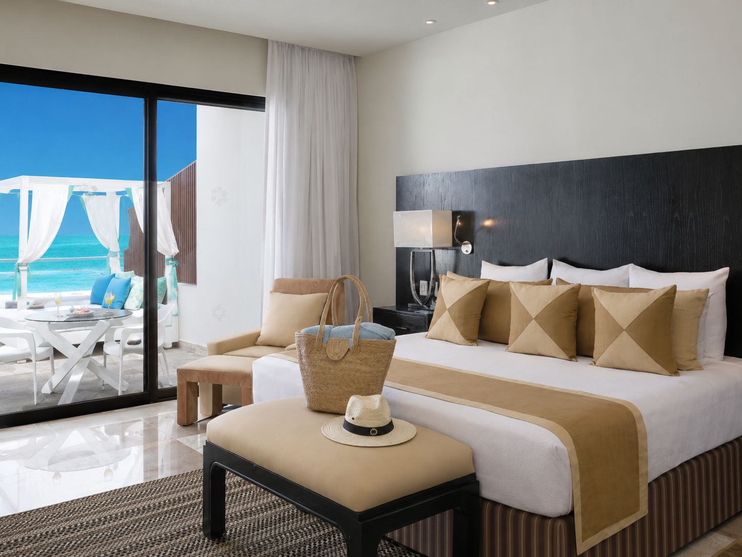 A hotel room with a bed, bedside table, lamp, and a view of the ocean through a large window.