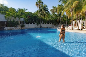 A swimming pool with clear blue water, surrounded by palm trees and a white building. - The Sens Riviera By Oasis (Akumal)