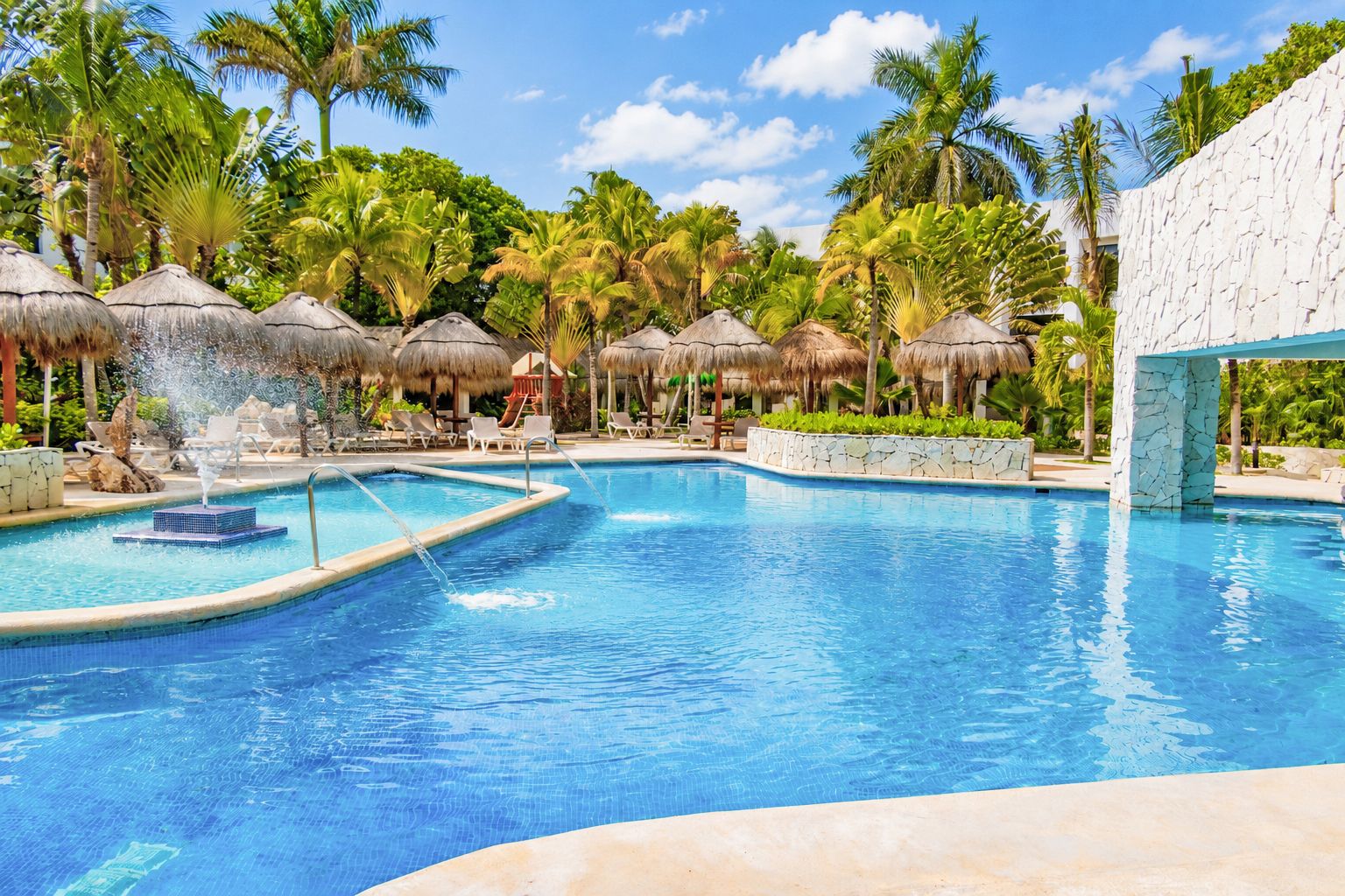 A resort pool with multiple lanes, lounge chairs, and thatched umbrellas.