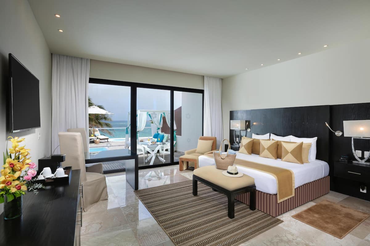 A modern hotel room with a large bed, a desk, a chair, and a view of the ocean.