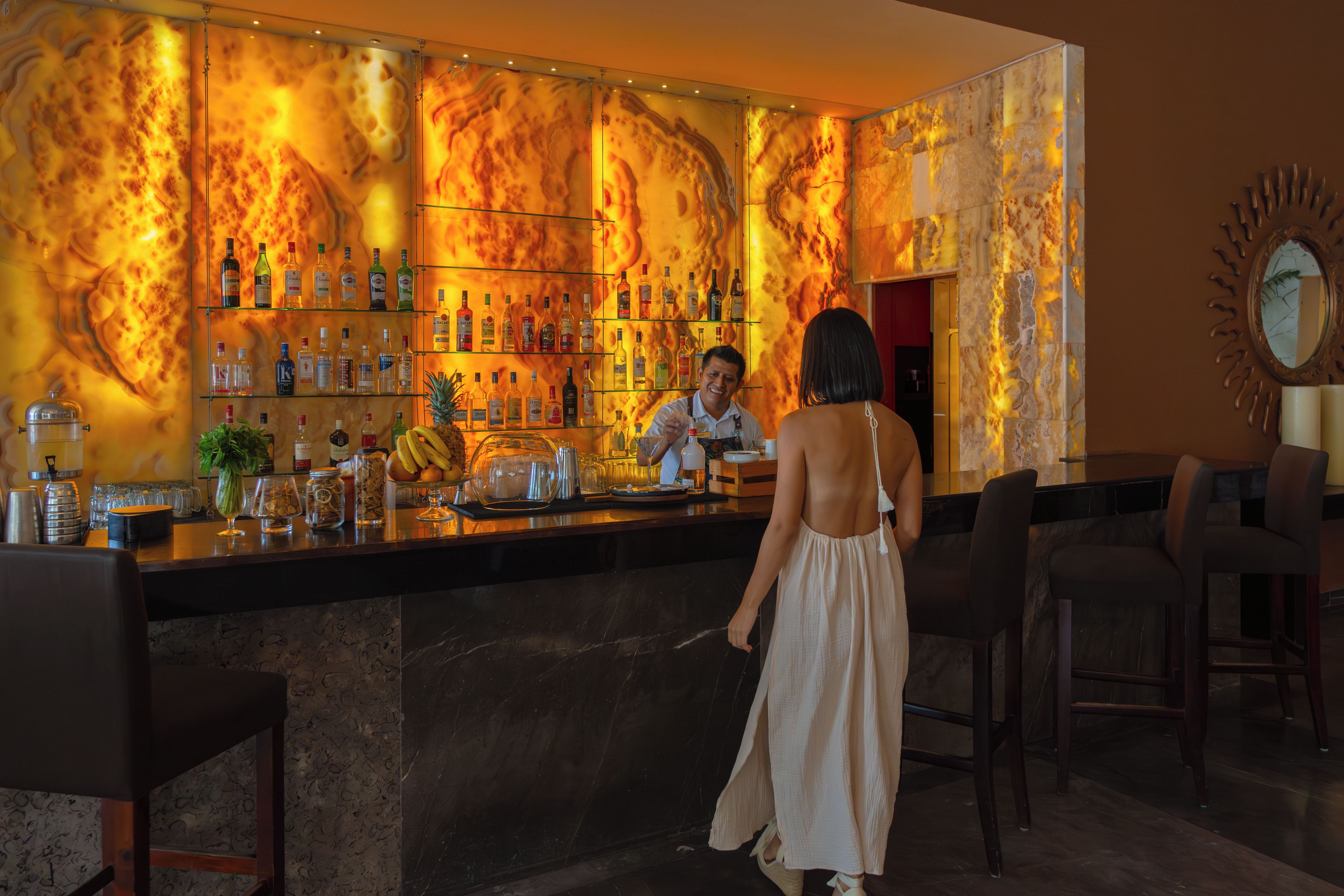 A bar area with a marble wall and a bartender serving a customer.