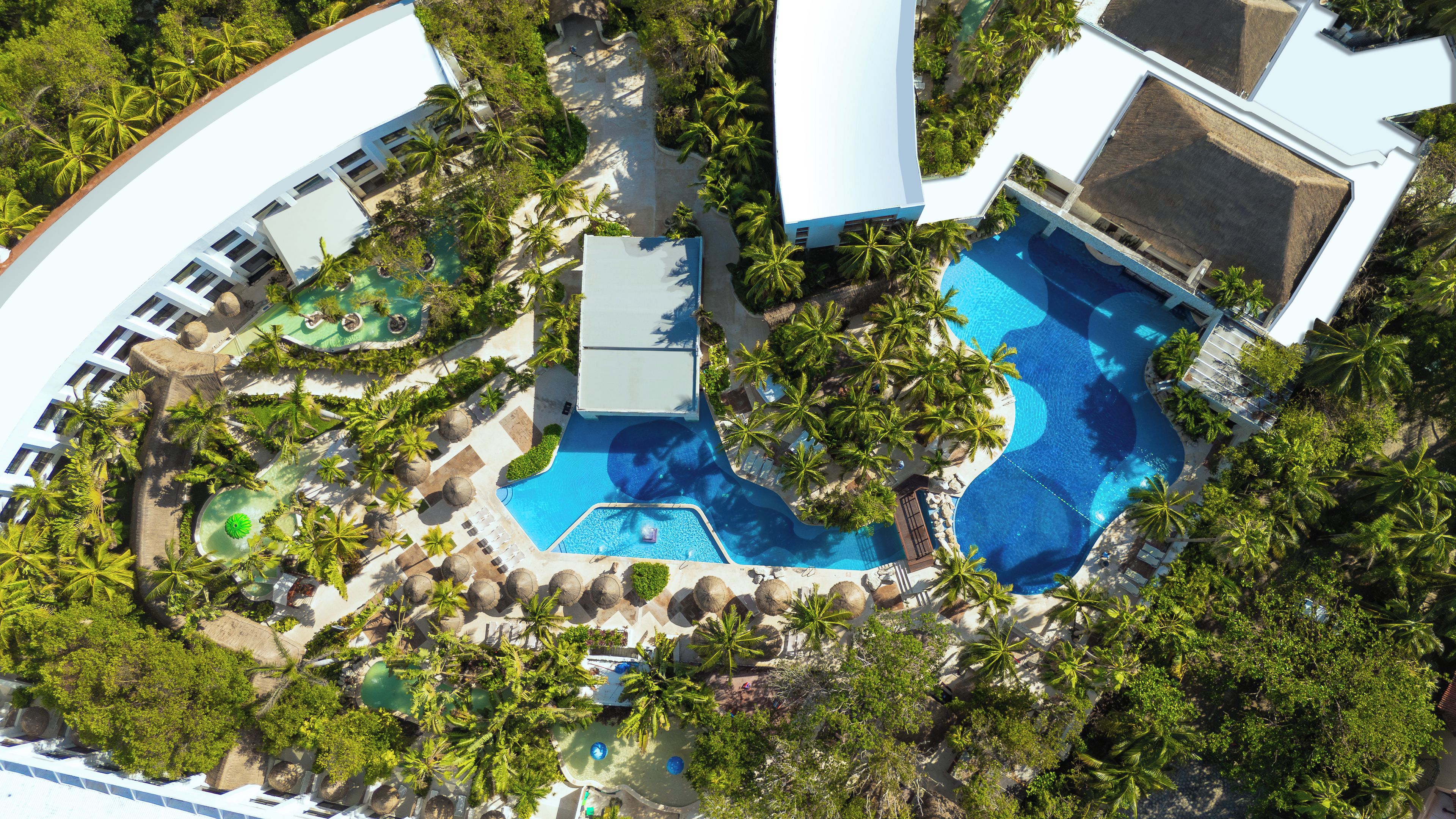Vista aérea de um resort com várias piscinas, cercado por palmeiras e áreas de lazer.