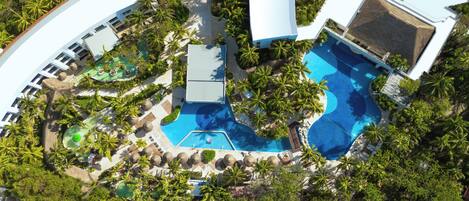 Vista aérea de un resort con múltiples piscinas rodeadas de palmeras y zonas de descanso.