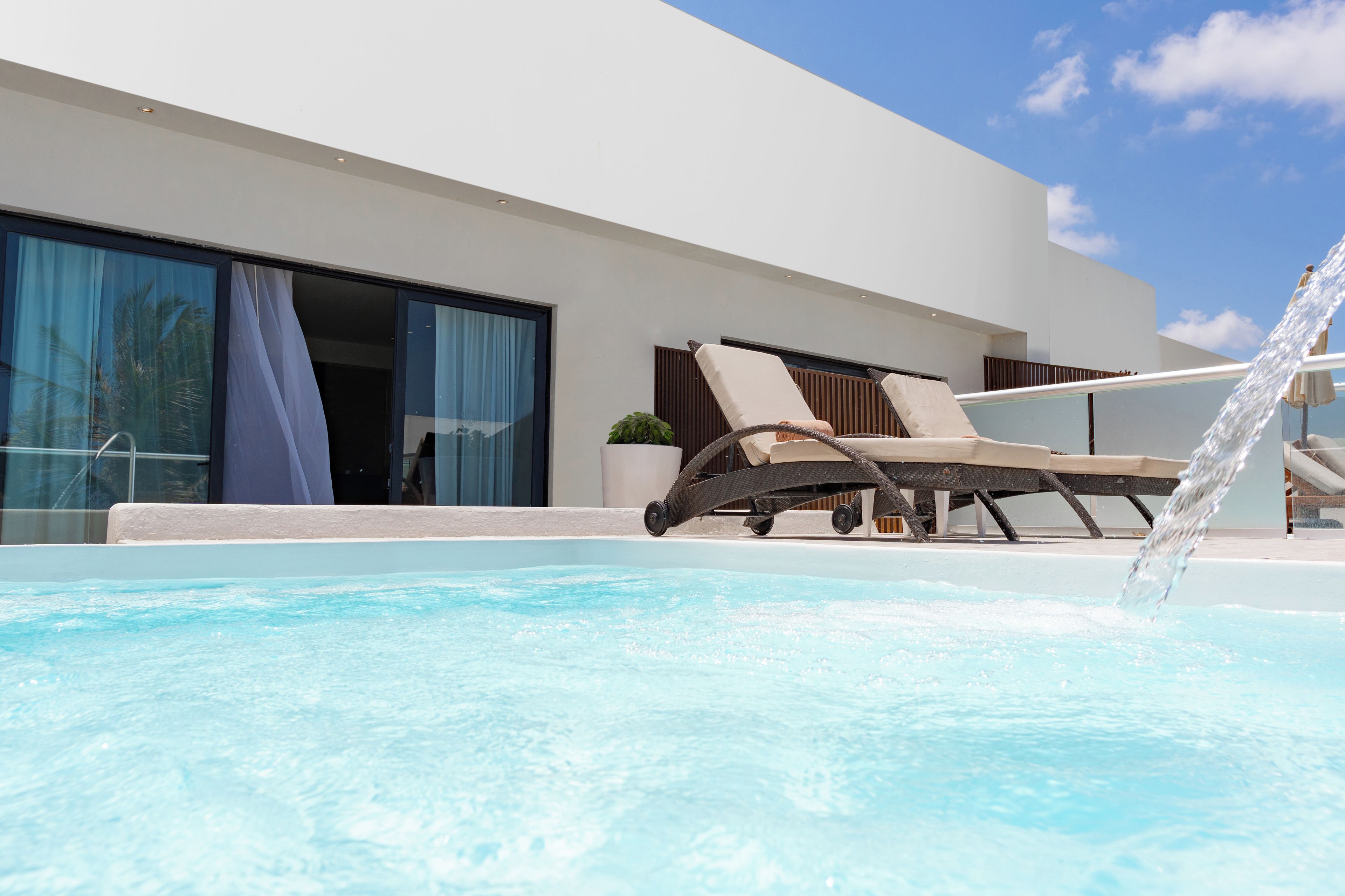 A modern hotel with a pool, lounge chairs, and a clear sky.