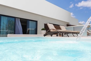 Ett modernt hotell med pool, solstolar och en klar himmel.