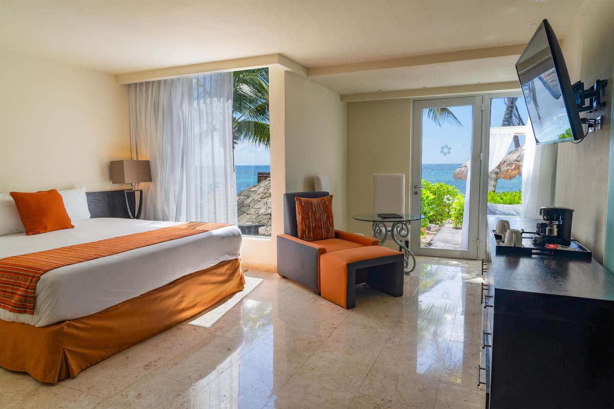 A hotel room with a bed, a small table, a sofa, a TV, and a view of the ocean.