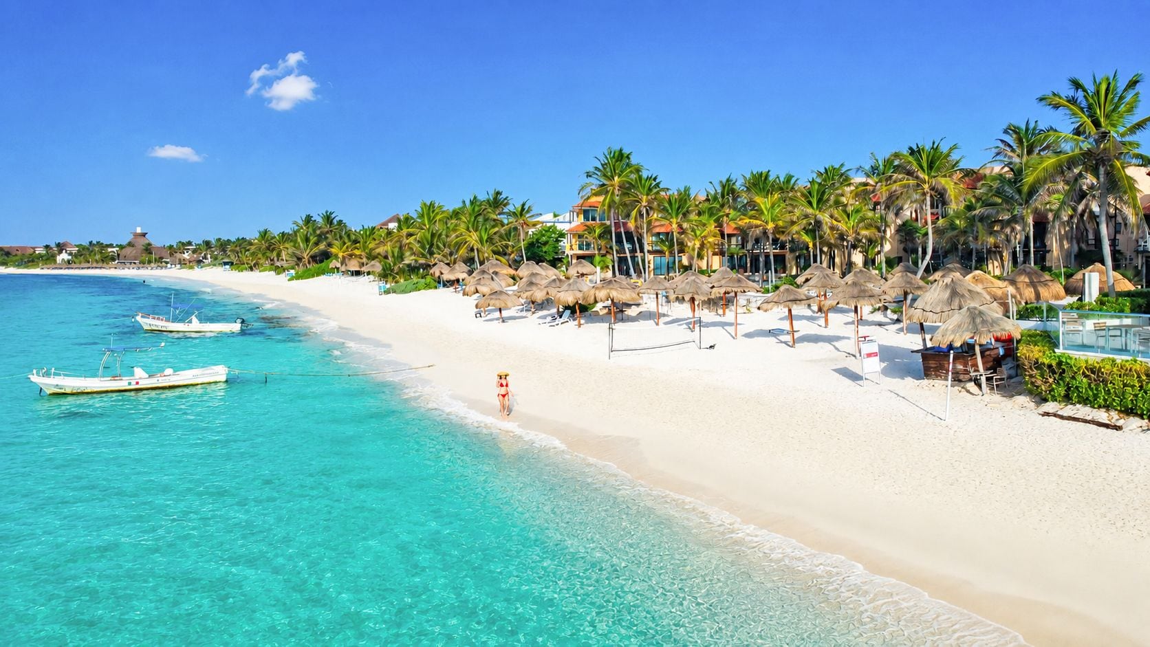 A beach resort with a clear turquoise sea, white sand, and palm trees.